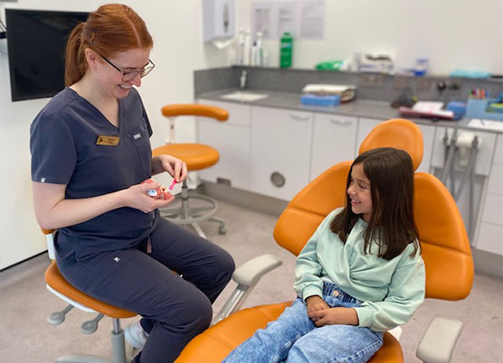 Dentist With Child Patient Showing Them How To Clean Their Teeth